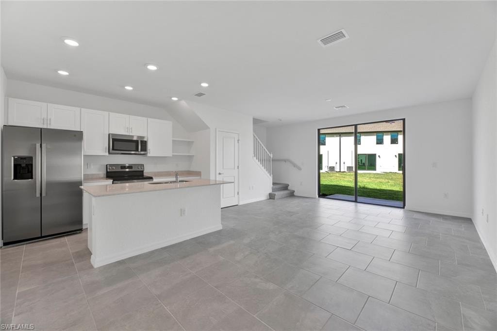 Kitchen featuring stainless steel appliances, white cabinets, a kitchen island with sink, open floor plan, and recessed lighting