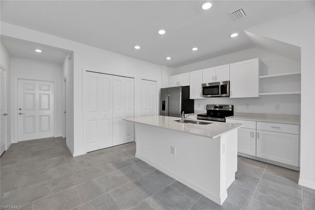Kitchen featuring white cabinets, open shelves, appliances with stainless steel finishes, recessed lighting, and a center island with sink