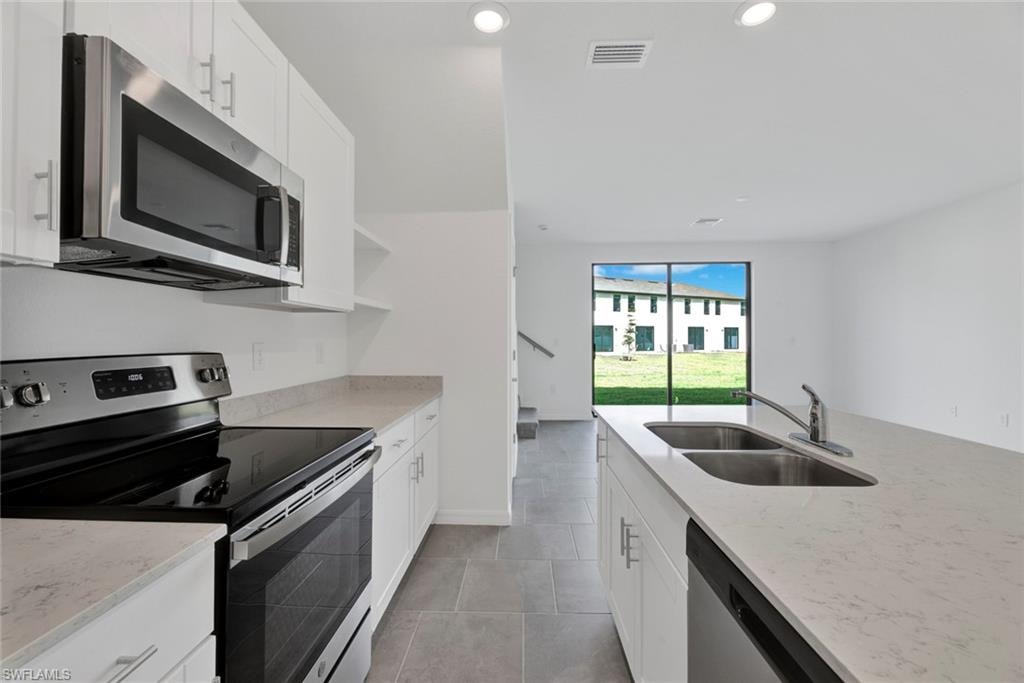 Kitchen featuring stainless steel appliances, white cabinets, light stone counters, and recessed lighting