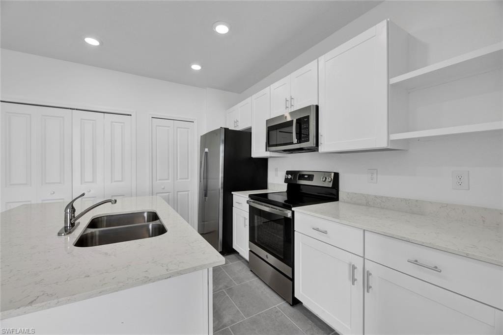 Kitchen featuring open shelves, stainless steel appliances, light stone counters, white cabinetry, and recessed lighting