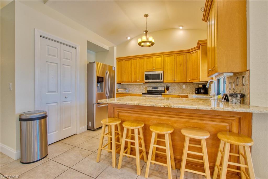 Kitchen with a peninsula, a breakfast bar, light stone countertops, stainless steel appliances, and tasteful backsplash