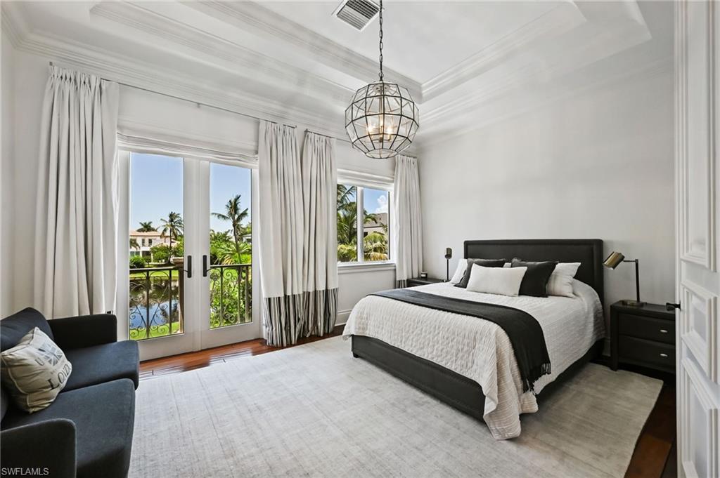 Bedroom with a raised ceiling, access to exterior, french doors, crown molding, and a chandelier