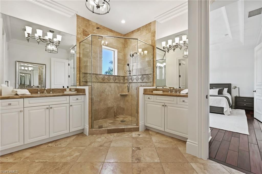 Bathroom featuring crown molding, two vanities, a stall shower, and ensuite bath