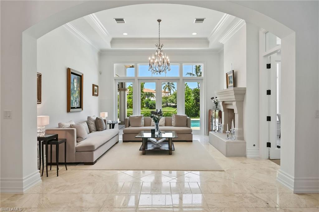 Living room featuring arched walkways, a towering ceiling, a chandelier, ornamental molding, and light marble finish flooring