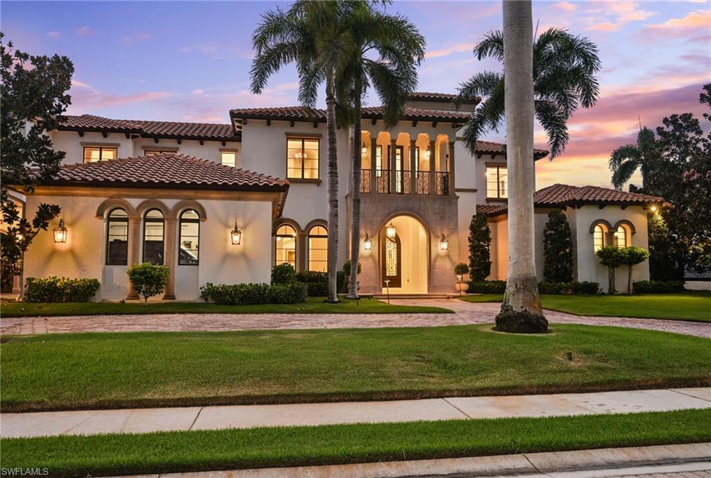 Mediterranean / spanish-style home featuring a balcony, stucco siding, a lawn, curved driveway, and a tile roof