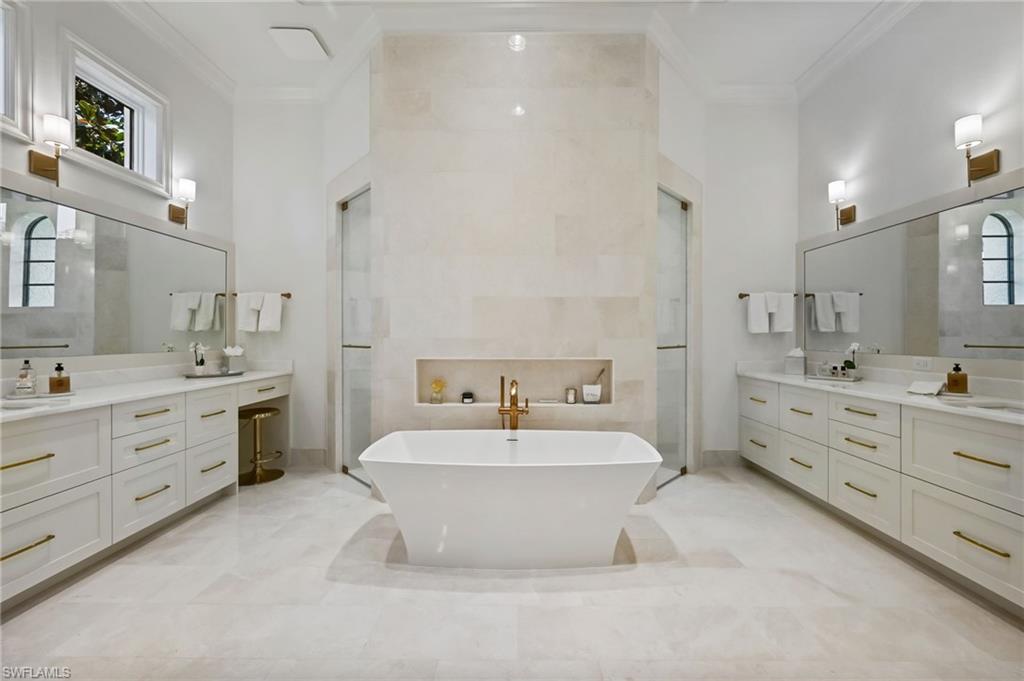 Full bath with ornamental molding, a freestanding bath, two vanities, walk in shower, and a towering ceiling