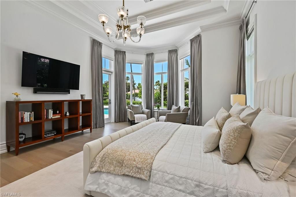 Bedroom with a raised ceiling, wood finished floors, crown molding, a chandelier, and access to outside