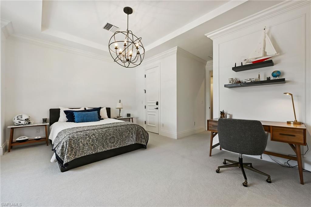 Bedroom with a tray ceiling, light carpet, ornamental molding, an office area, and a chandelier
