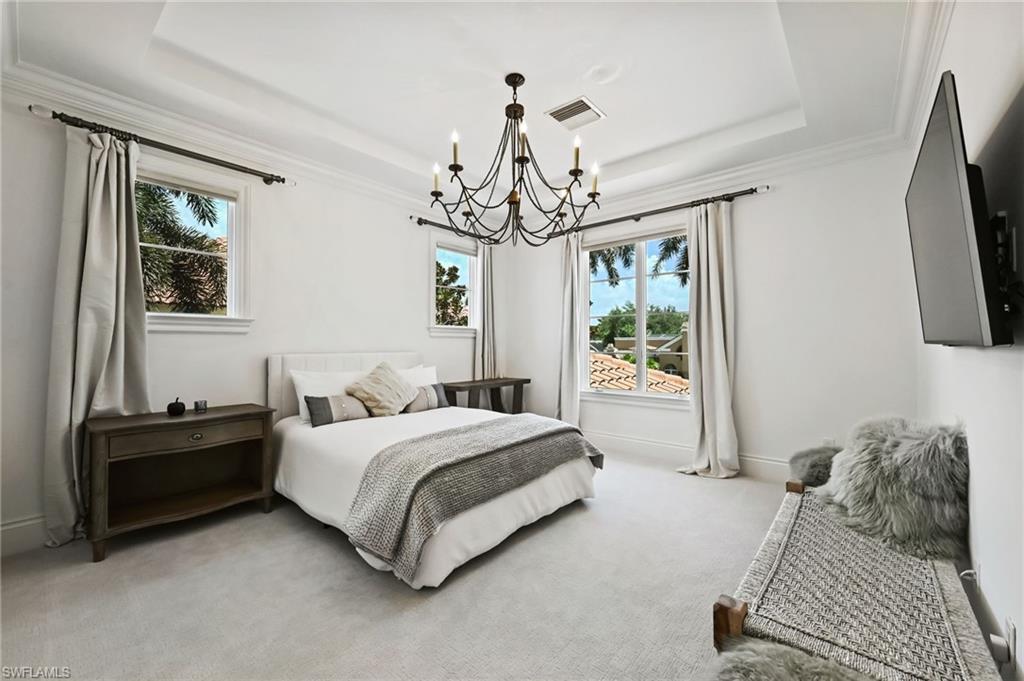 Carpeted bedroom featuring a tray ceiling, ornamental molding, and a chandelier