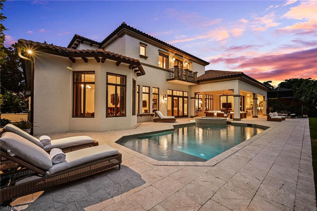 Back of house at dusk featuring an outdoor living space, stucco siding, a pool with connected hot tub, a patio area, and a balcony