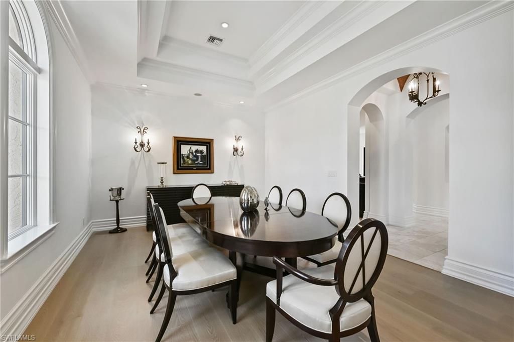 Dining space featuring light wood-type flooring, ornamental molding, a tray ceiling, arched walkways, and a chandelier