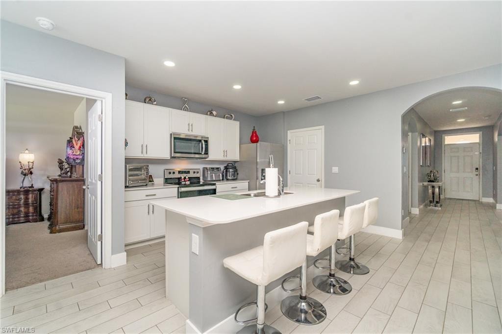 Kitchen featuring stainless steel appliances, light countertops, a kitchen bar, white cabinetry, and arched walkways