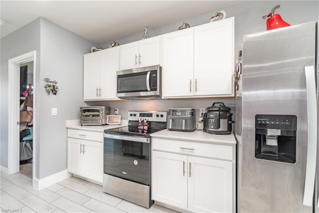 Kitchen with appliances with stainless steel finishes, white cabinets, and light tile patterned floors