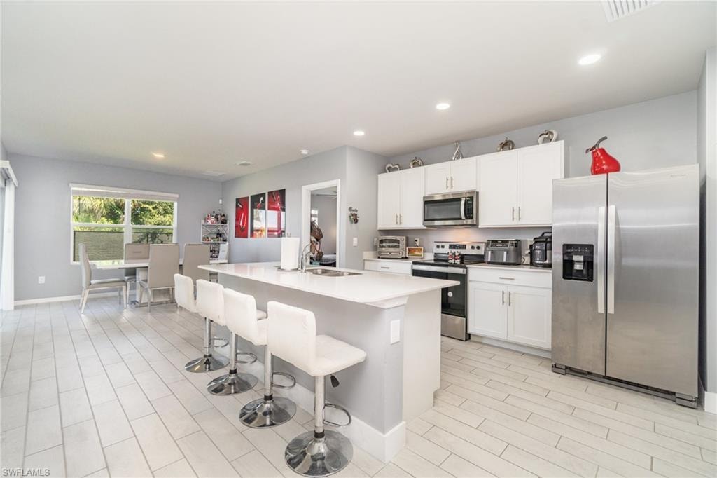 Kitchen featuring appliances with stainless steel finishes, a breakfast bar, a center island with sink, recessed lighting, and wood finish floors