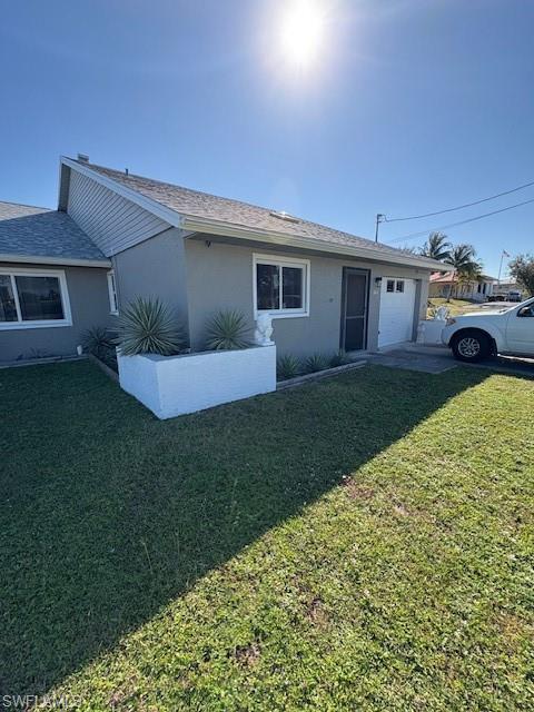 Ranch-style home with stucco siding, an attached garage, a front yard, and roof with shingles
