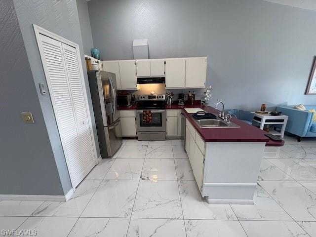 Kitchen with dark countertops, a peninsula, appliances with stainless steel finishes, white cabinetry, and open floor plan