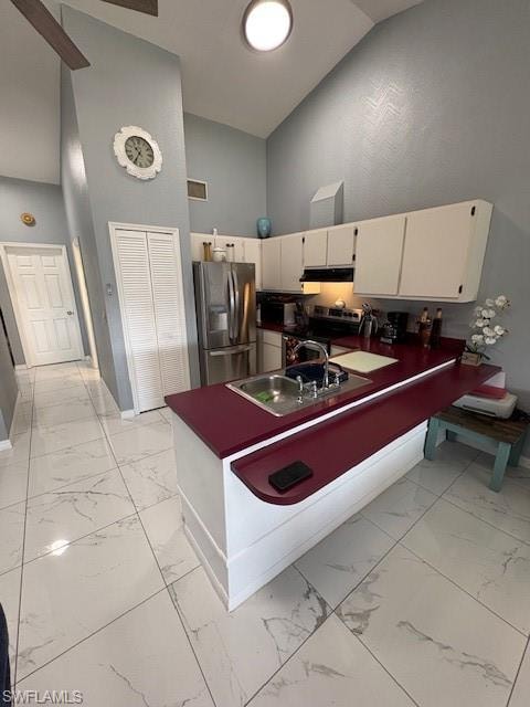 Kitchen with high vaulted ceiling, fridge, a peninsula, light marble finish flooring, and dark countertops