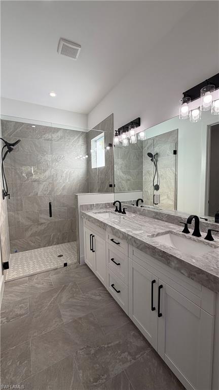 Bathroom featuring a marble finish shower, double vanity, and dark marble finish floors