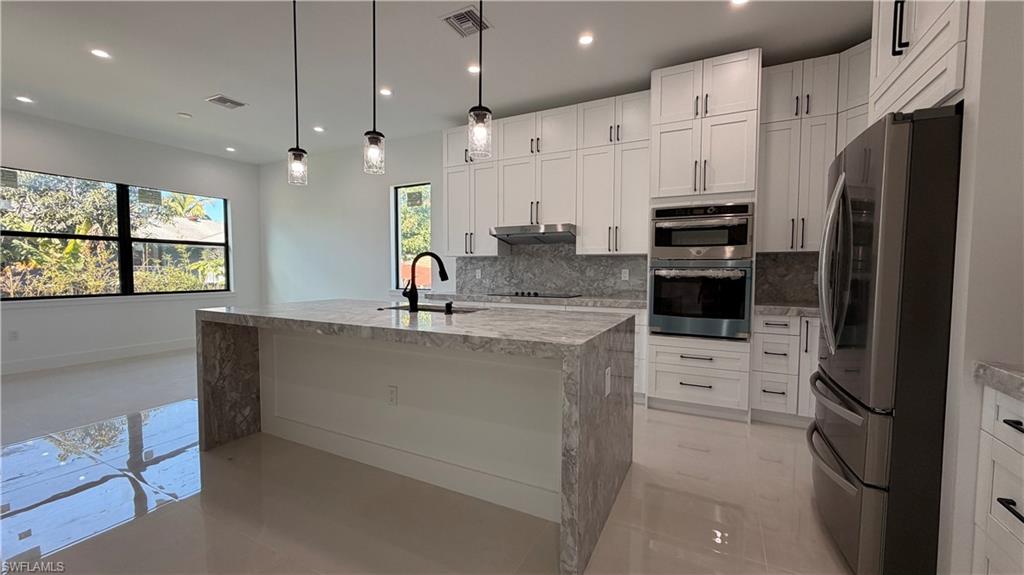 Kitchen with appliances with stainless steel finishes, light stone countertops, decorative backsplash, pendant lighting, and recessed lighting