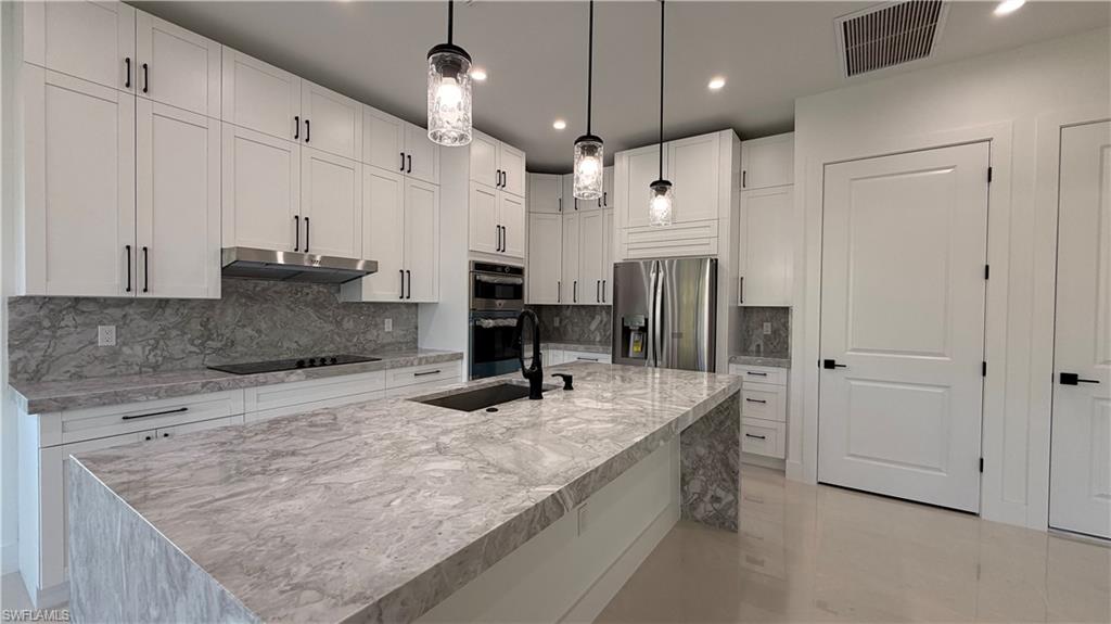 Kitchen featuring appliances with stainless steel finishes, recessed lighting, light stone countertops, white cabinetry, and a center island with sink