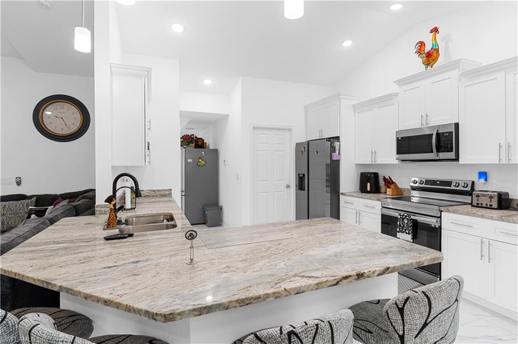 Kitchen featuring a breakfast bar area, a peninsula, appliances with stainless steel finishes, light stone counters, and recessed lighting