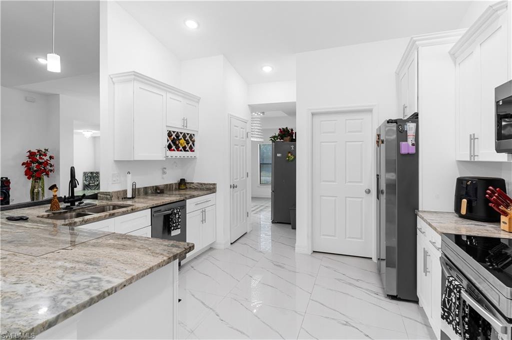 Kitchen featuring white cabinetry, appliances with stainless steel finishes, light marble finish flooring, hanging light fixtures, and light stone counters