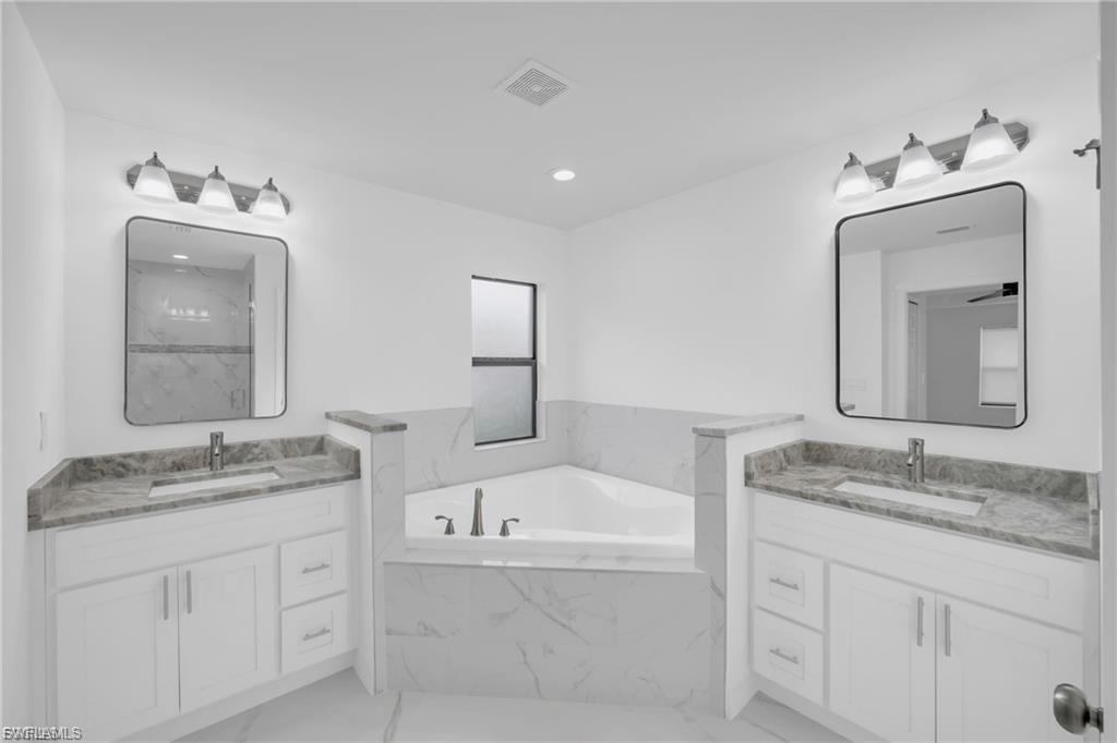Full bathroom featuring two vanities, a bath, light marble finish floors, recessed lighting, and a marble finish shower