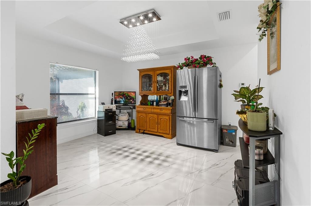 Kitchen with a tray ceiling, stainless steel fridge, brown cabinetry, and light marble finish floors