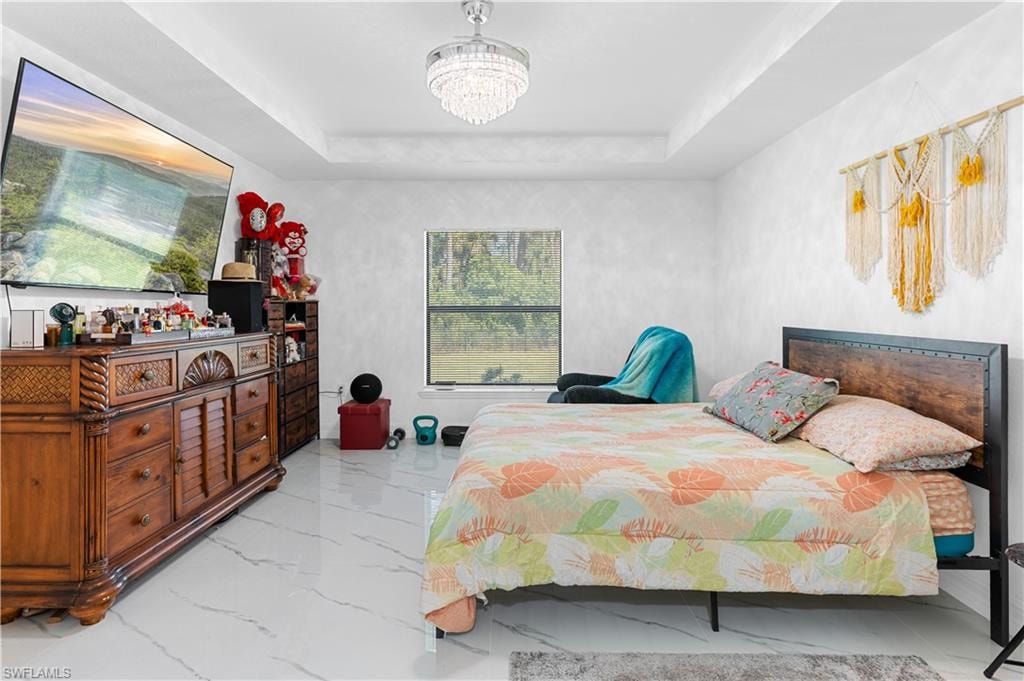 Bedroom featuring a tray ceiling, light marble finish flooring, and a chandelier