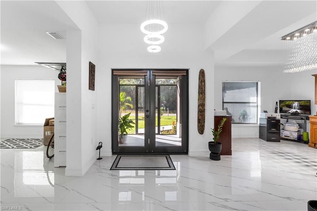 Foyer with a chandelier, light marble finish floors, and french doors