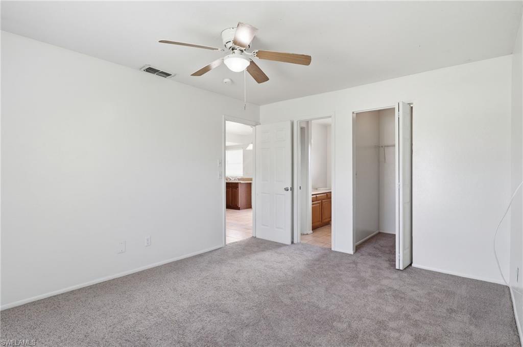 Unfurnished bedroom featuring a walk in closet, light colored carpet, and ceiling fan