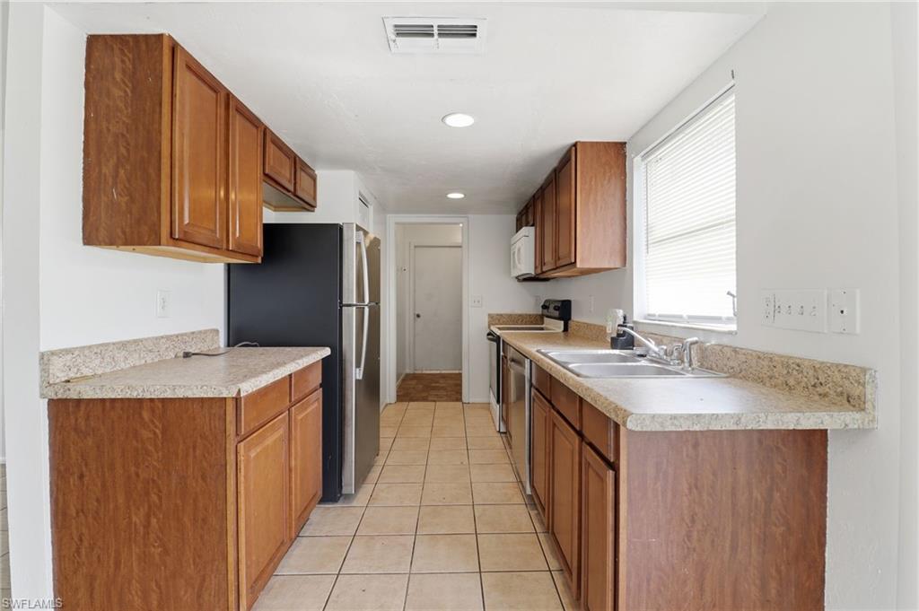 Kitchen featuring brown cabinetry, stainless steel appliances, light tile patterned floors, recessed lighting, and light countertops