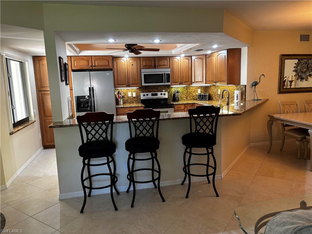 Kitchen with dark stone countertops, appliances with stainless steel finishes, backsplash, a peninsula, and brown cabinetry