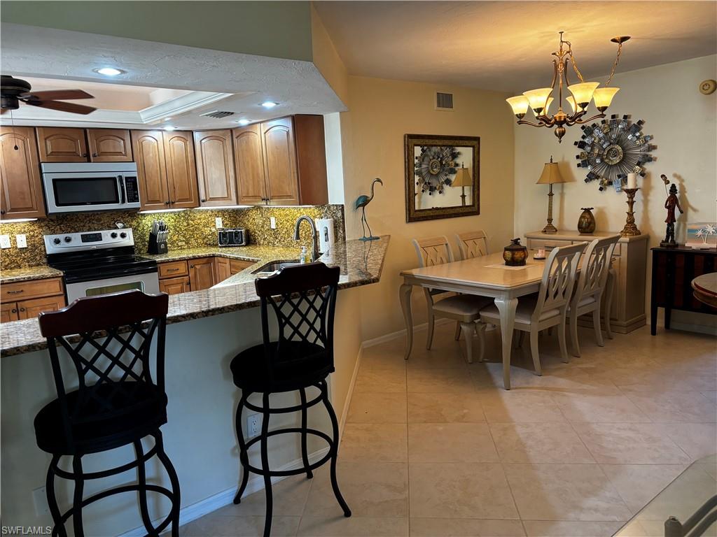 Kitchen featuring dark stone countertops, appliances with stainless steel finishes, a kitchen bar, tasteful backsplash, and brown cabinetry