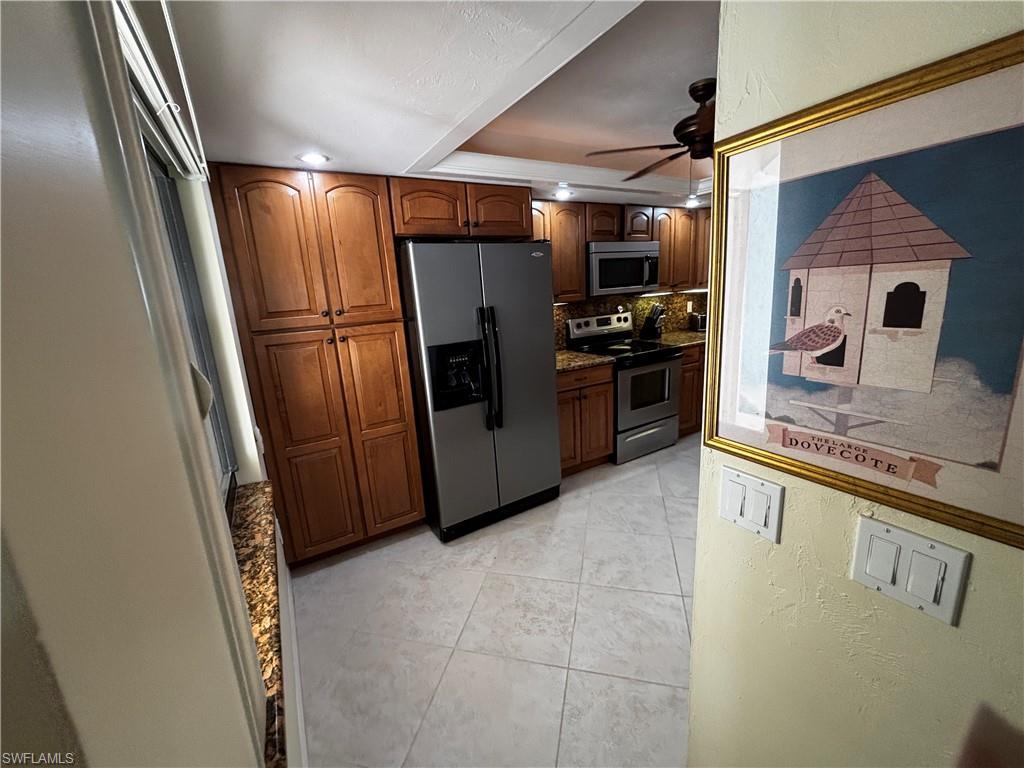 Kitchen featuring stainless steel appliances, brown cabinets, a ceiling fan, light tile patterned floors, and a tray ceiling