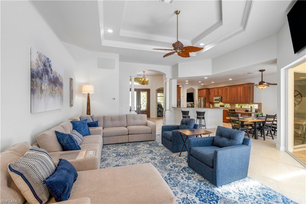 Living area featuring a ceiling fan, recessed lighting, arched walkways, a raised ceiling, and light tile patterned floors
