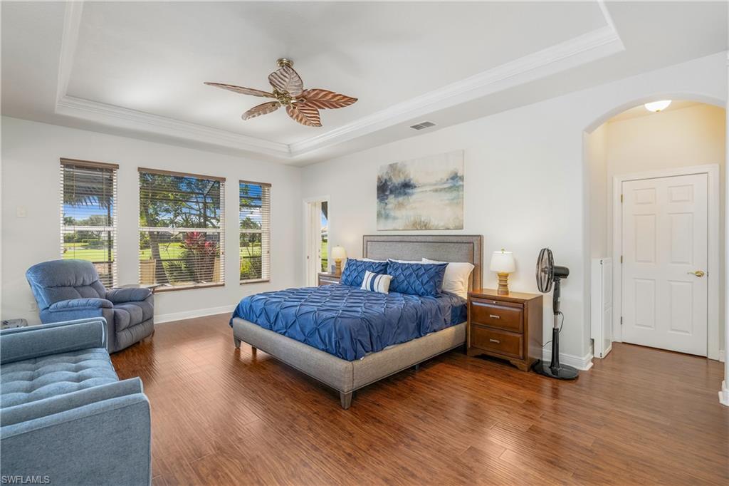 Bedroom with a tray ceiling, wood finished floors, arched walkways, crown molding, and ceiling fan
