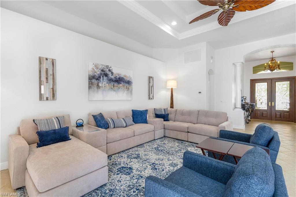 Tiled living room featuring a tray ceiling, arched walkways, french doors, recessed lighting, and ornamental molding