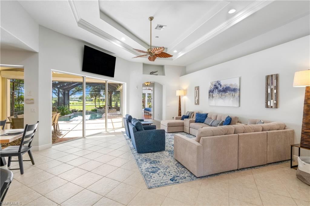 Living area featuring a tray ceiling, recessed lighting, light tile patterned floors, a high ceiling, and ceiling fan