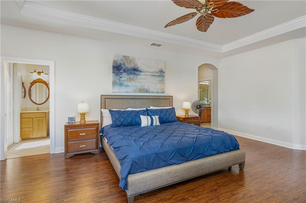 Bedroom with connected bathroom, crown molding, wood finished floors, arched walkways, and ceiling fan
