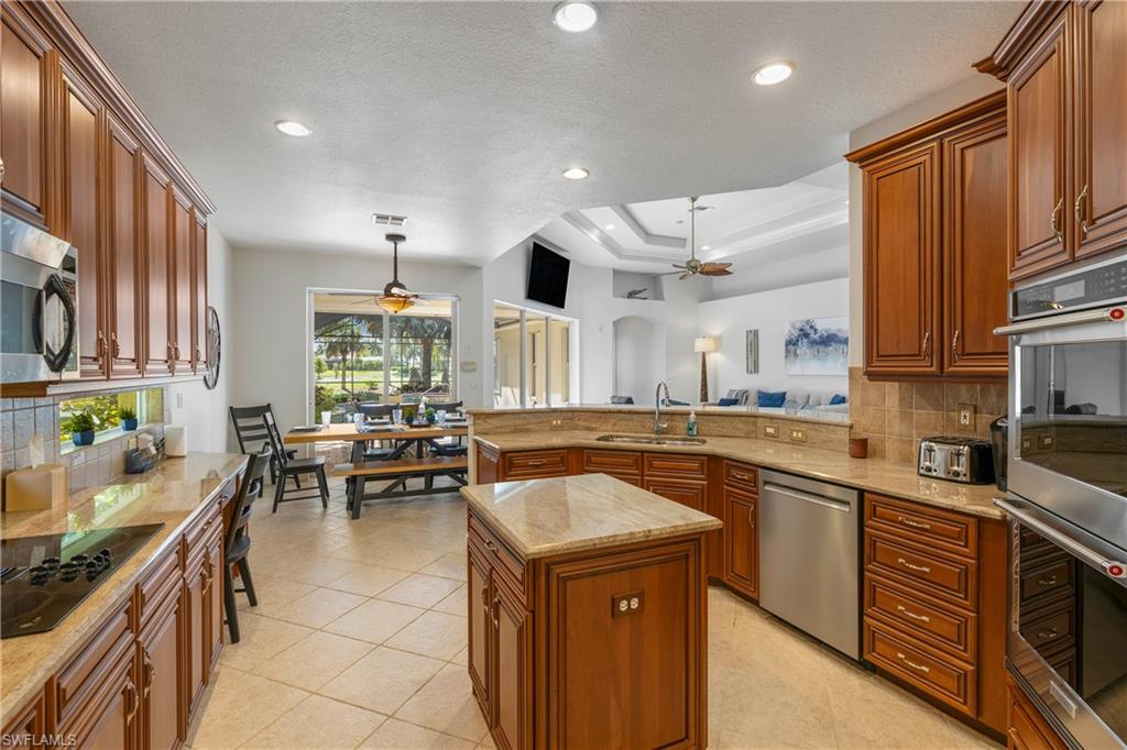 Kitchen with tasteful backsplash, stainless steel appliances, a ceiling fan, brown cabinetry, and recessed lighting