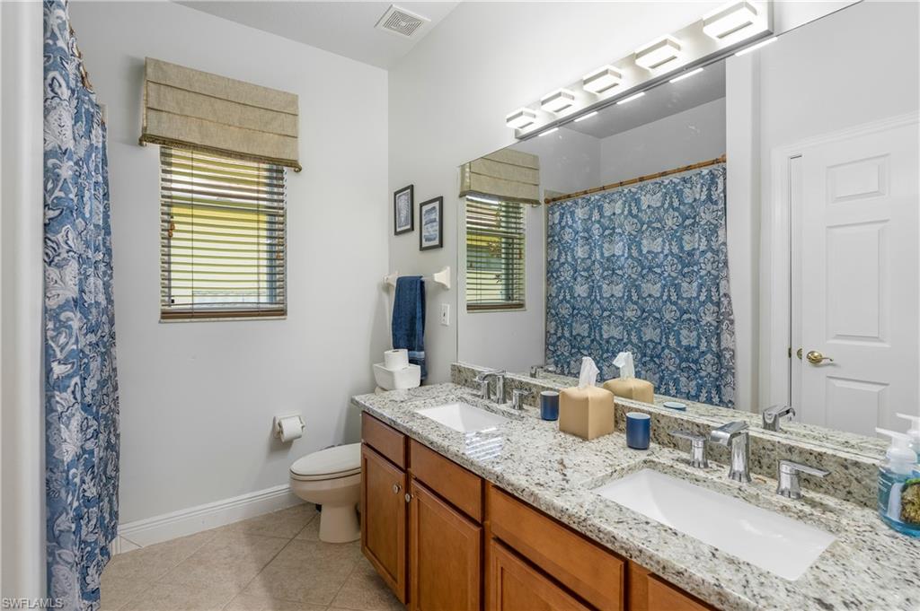Full bath with double vanity, plenty of natural light, curtained shower, and light tile patterned flooring
