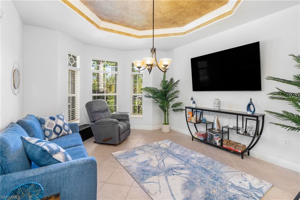 Living room with a raised ceiling, light tile patterned flooring, a chandelier, and ornamental molding