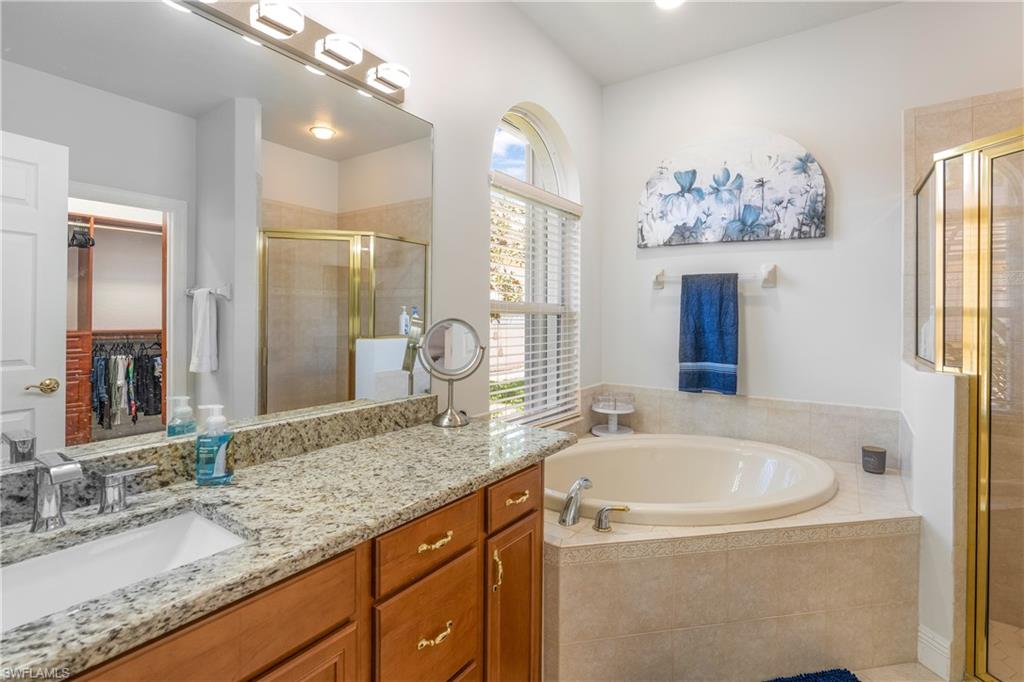 Full bathroom with vanity, a walk in closet, a garden tub, and a stall shower