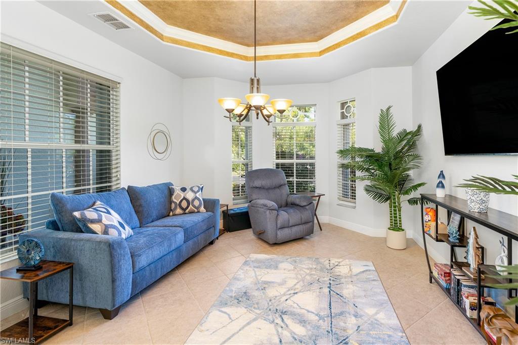 Living room featuring a tray ceiling, ornamental molding, a chandelier, and light tile patterned flooring