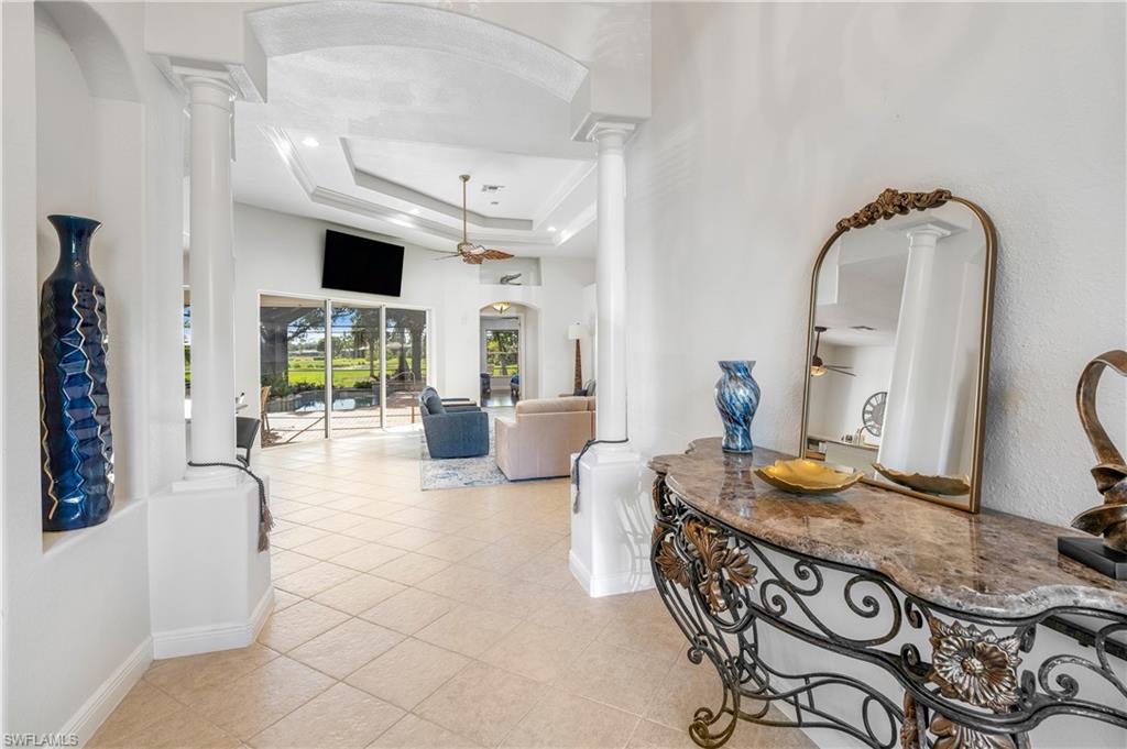 Hall featuring arched walkways, a tray ceiling, light tile patterned flooring, and decorative columns