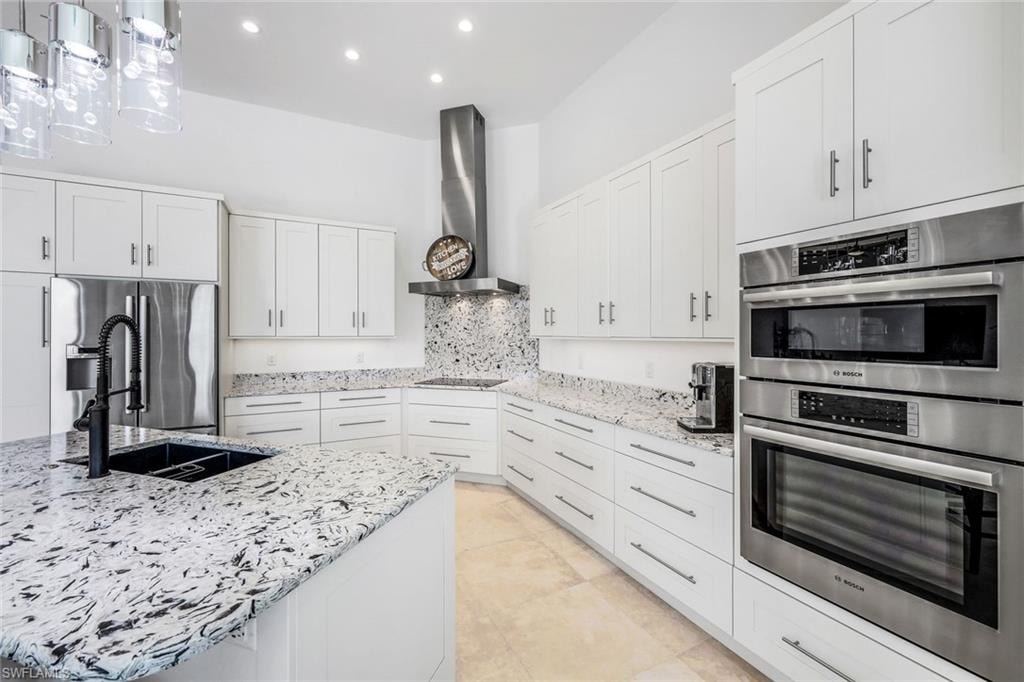 Kitchen with appliances with stainless steel finishes, white cabinets, light stone countertops, hanging light fixtures, and recessed lighting