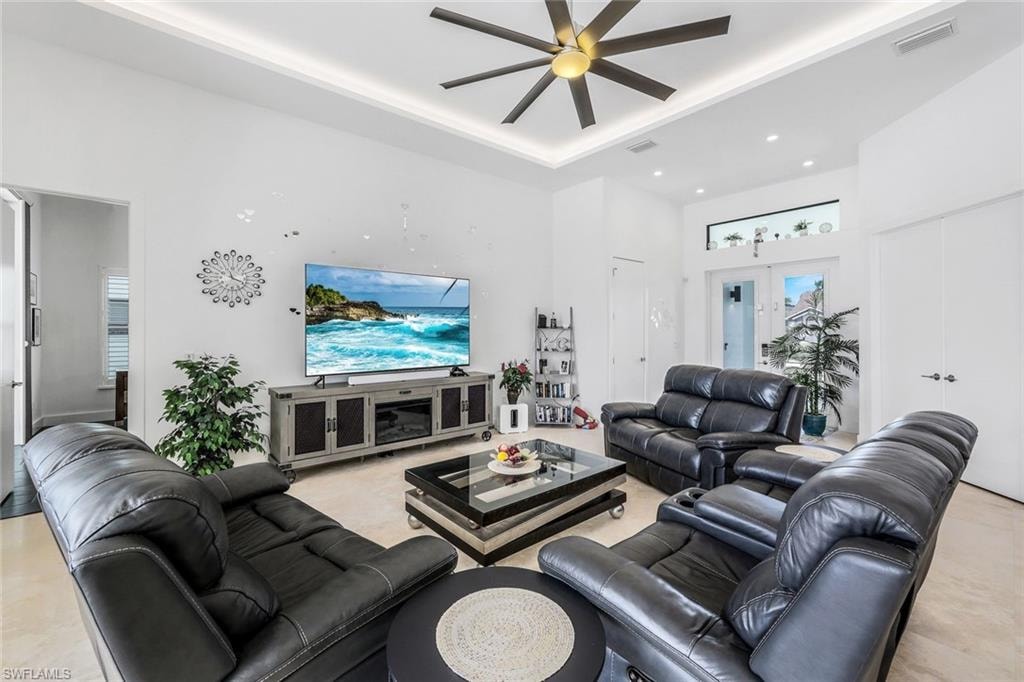 Living room with a high ceiling, a ceiling fan, recessed lighting, a tray ceiling, and french doors