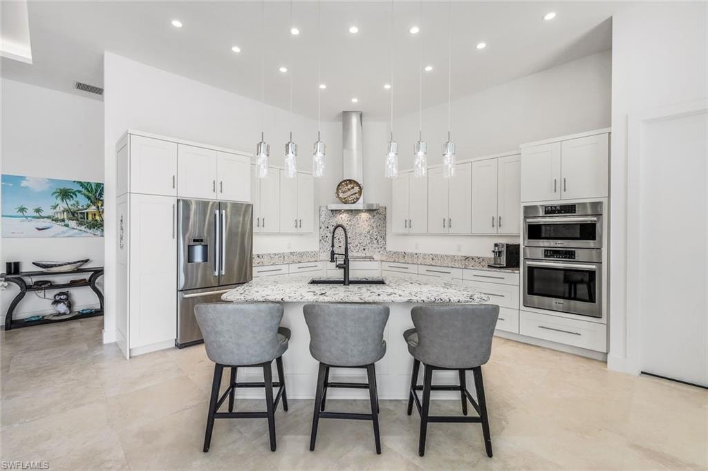 Kitchen with a towering ceiling, backsplash, a kitchen bar, white cabinets, and hanging light fixtures