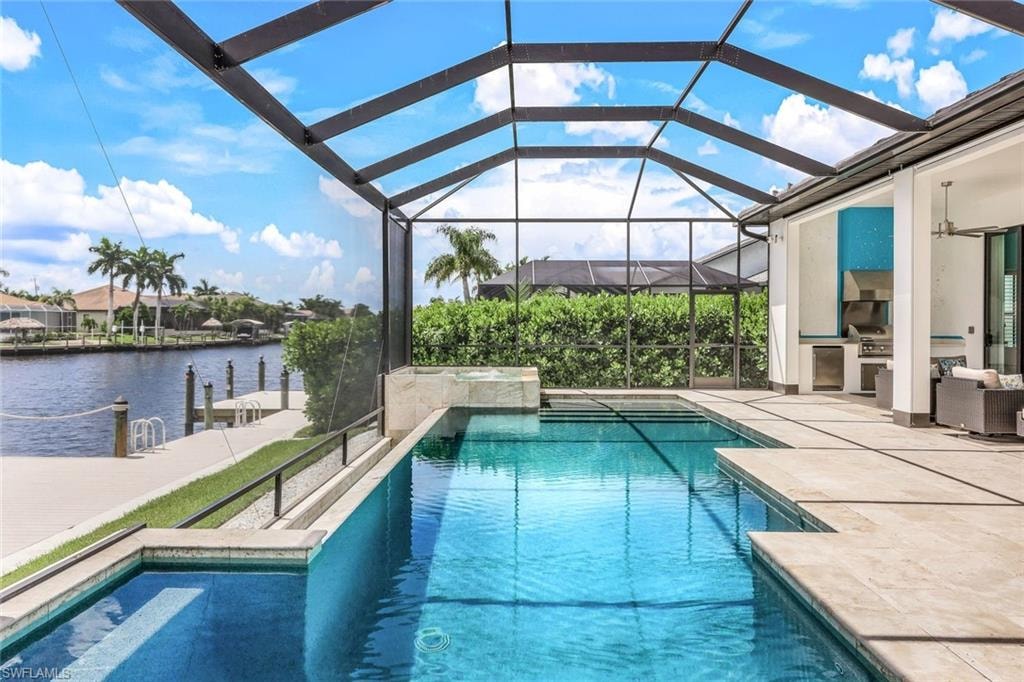 View of pool featuring exterior kitchen, a patio area, glass enclosure, a sunroom, and a water view